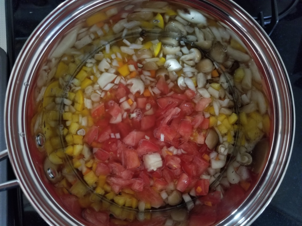 鍋で煮込まれる野菜とトマトとコンソメ
